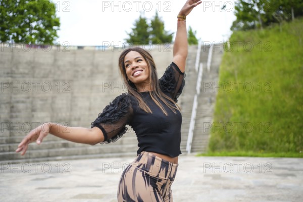 Latin smiling young woman enjoying dancing salsa alone in a park