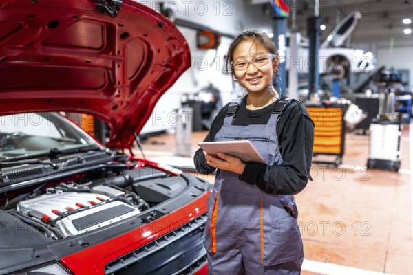 Confident female mechanic using a digital tablet, inspecting a car engine in a professional auto repair shop