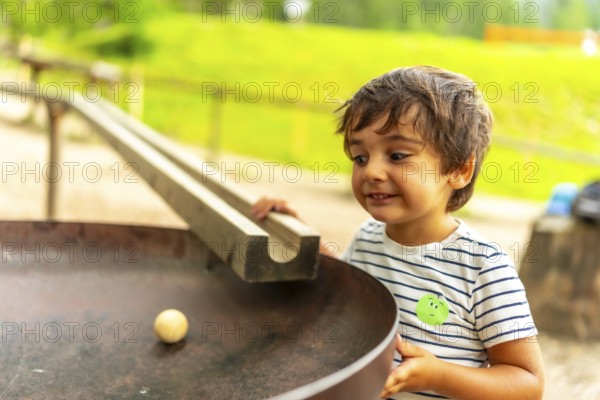 Curious child having fun with a wooden ball rolling down a track in a playground, learning about gravity and physics