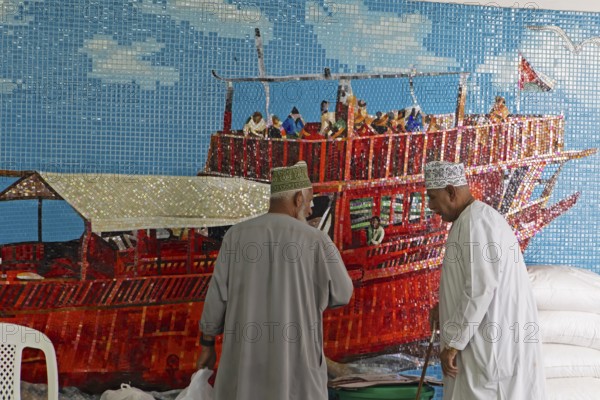 Omani men in dishdashas in front of the wall mosaic of a ship in Muttrah Fish Market, Muscat, Oman, Asia