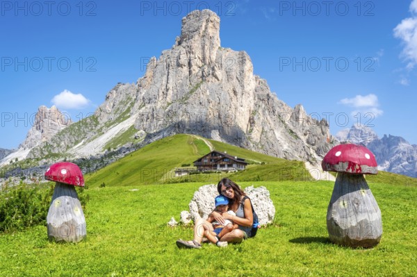 Mother and child relaxing near wooden mushrooms, enjoying breathtaking view of giau pass and surrounding dolomites peaks on sunny summer day