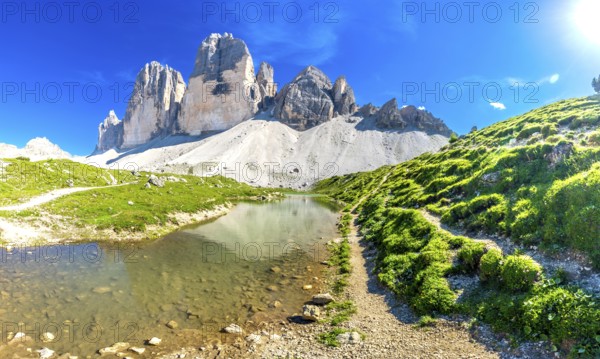 Breathtaking panorama of tre cime di lavaredo reflecting in a crystal clear alpine lake, surrounded by lush meadows on a sunny day