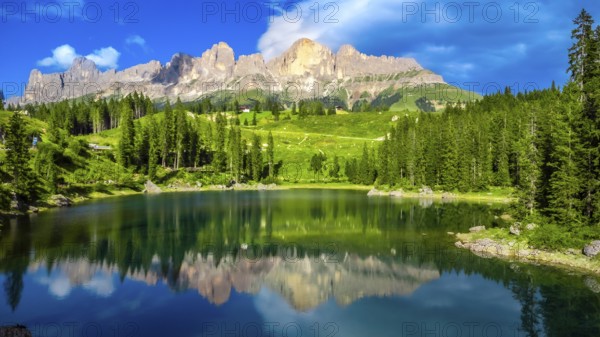 Stunning view of latemar mountain group reflecting in the emerald smooth water of lake carezza on a sunny summer day, dolomites, italian alps