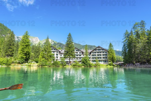 Wooden oar stroking emerald green water of lake braies, with hotel pragser wildsee and dolomites mountains reflected in the tranquil surface
