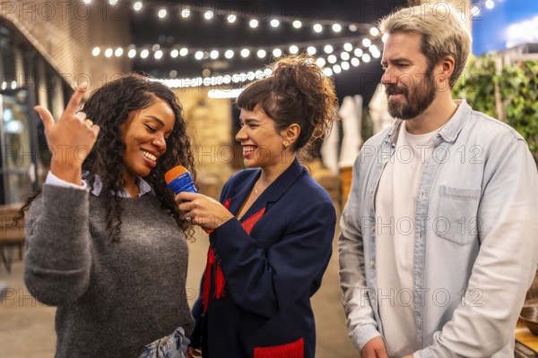 Multi-ethnic happy friends enjoying singing karaoke together at night outdoor party in the terrace of a bar