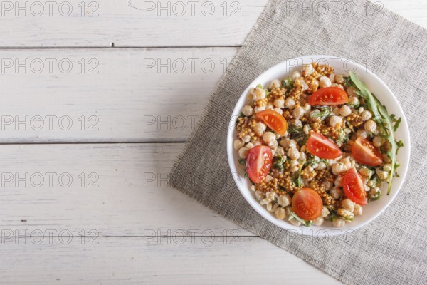 Vegetarian salad of boiled chickpeas, cheese, arugula, mustard and cherry tomatoes on white wooden background. copy space, top view