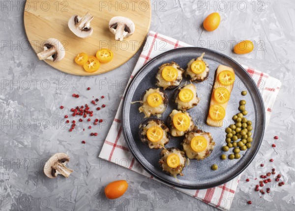 Stuffed fried champignons with cheese, kumquats and green peas on a gray concrete background. ceramic plate, top view, flat lay, close up, horizontal