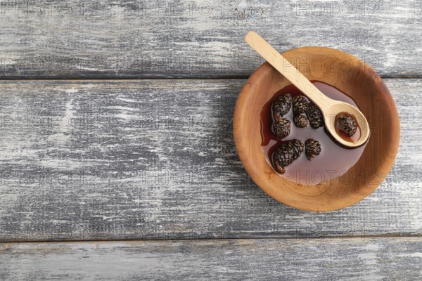 Pine cone jam in wooden bowl on gray wooden background. Top view, flat lay, copy space