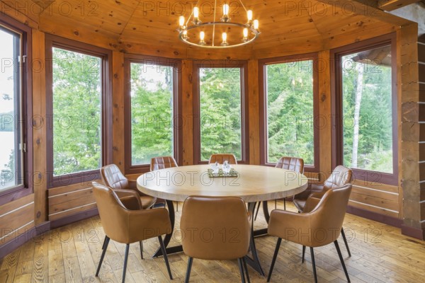 Round wooden dining table with tan leather armchairs in dining room inside a milled Eastern white pine timber and flat log profile home, Quebec, Canada, North America