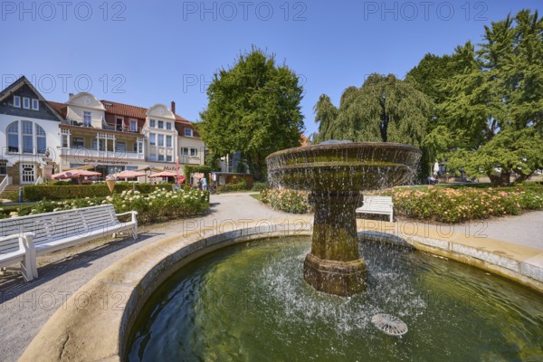 Fountain with benches, trees and houses under a cloudless blue sky in Bad Salzuflen, Lippe district, North Rhine-Westphalia, Germany, Europe