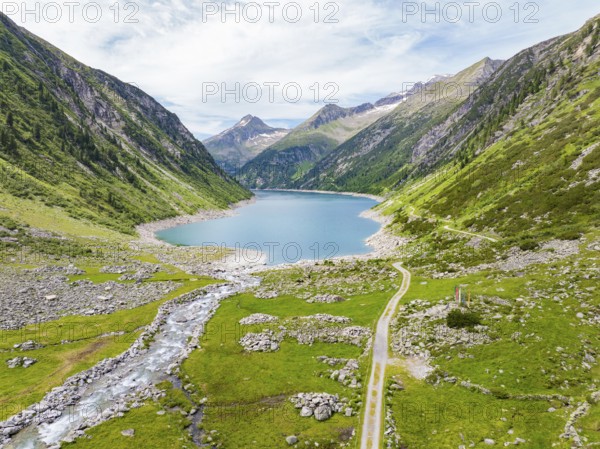 An idyllic mountain lake surrounded by high peaks and green meadows under a blue sky, Klein Tibet, Zillertal, Austria, Europe