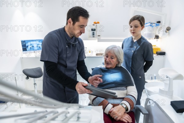 Dentist and nurse explaining radiography to a senior patient sitting in a dental chair, during a consultation in a dental clinic