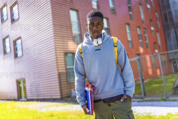 Cool african student with hoodie and rucksack holding folders outside the university