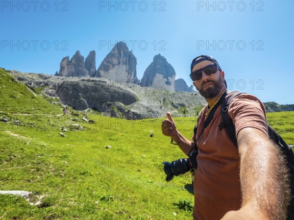 Photographer taking a selfie while hiking showing thumbs up sign with tre cime di lavaredo mountains in the background