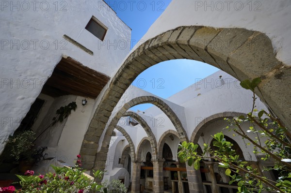 Inner courtyard with stone arches, plants and white walls under a blue sky in a Mediterranean atmosphere, Agiou Theologou Monastery, St John's Monastery, Chora, Patmos, Dodecanese, Greek Islands, Greece, Europe