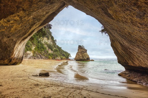 Looking out of a cave onto a rock formation and a quiet beach, Cathedral Grove, Coromandel, New Zealand, Oceania