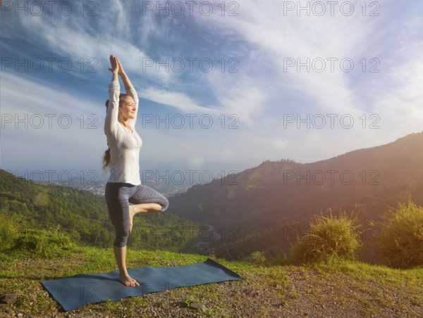 Yoga practice outdoors, woman practices balance yoga asana Vrikshasana tree pose in Himalayas mountains outdoors in the morning. Himachal Pradesh, India, Asia