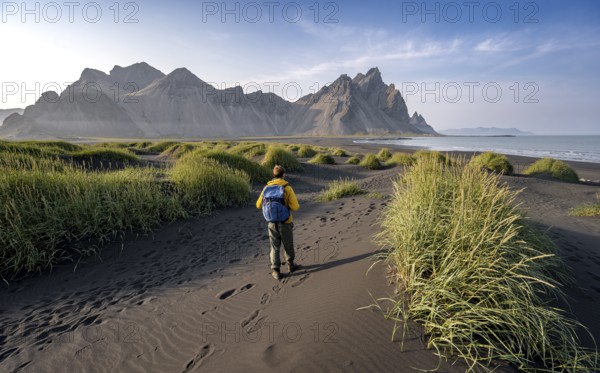 Tourist on a sand dune, Black beach with volcanic sand, Sand beach, Dunes with grass, Stokksnes headland, Klifatindur mountain range, Austurland, East Iceland, Iceland, Europe