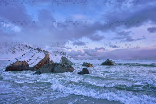 Waves of Norwegian sea on rocky coast in fjord on sunset with sun. Skagsanden beach, Lofoten islands, Norway, Europe