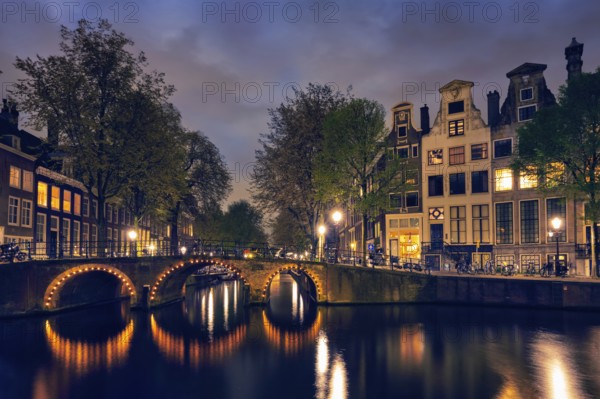 Night view of Amterdam cityscape with canal, bridge and medieval houses in the evening twilight illuminated. Amsterdam, Netherlands