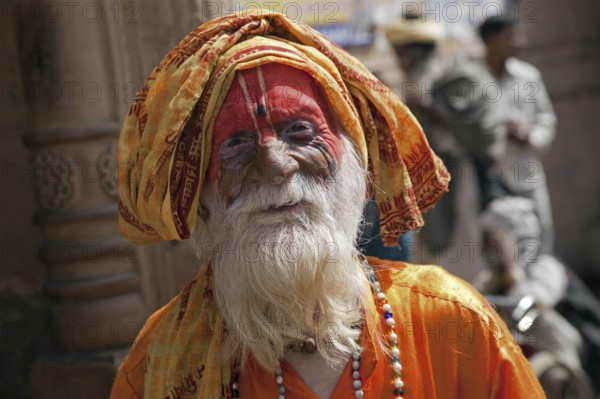 Old Hare Krishna follower dressed in orange dress in front of temple in Govardhan, India, Asia