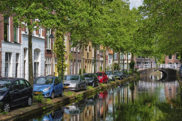 Delft, Netherlands, May 12, 2017: Cars and bicycles parked on canal embankment in street of Delft with reflection. Delft, Netherlands