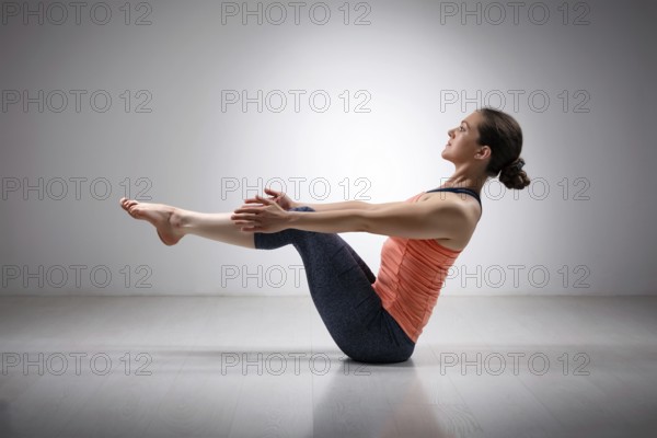 Beautiful sporty fit yogini woman practices yoga asana Paripurna navasana, boat pose beginner variation