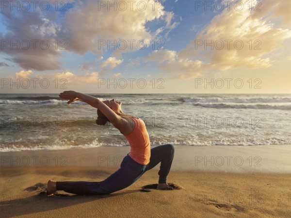 Yoga outdoors, sporty fit woman practices yoga Anjaneyasana, low crescent lunge pose outdoors at beach on sunset
