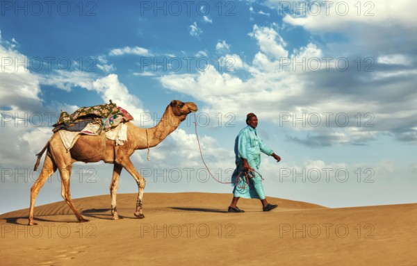 Rajasthan travel background, Indian cameleer (camel driver) with camels in dunes of Thar desert. Jaisalmer, Rajasthan, India, Asia
