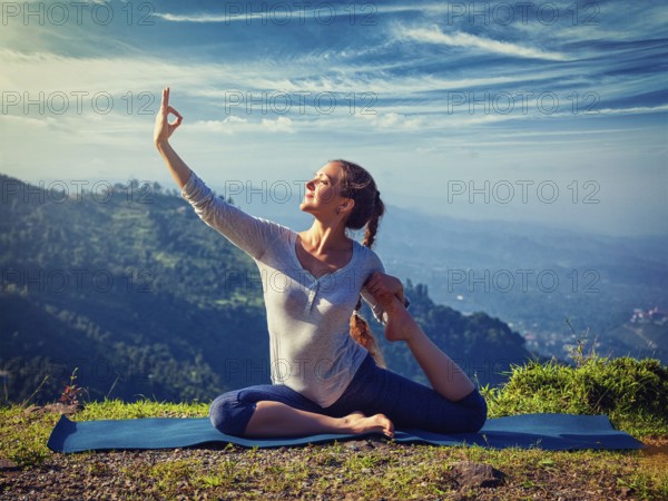 Yoga outdoors, young sporty fit woman doing stretching yoga asana Eka pada rajakapotasana, one-legged king pigeon pose in Himalayas mountains, India. Vintage retro effect filtered hipster style image