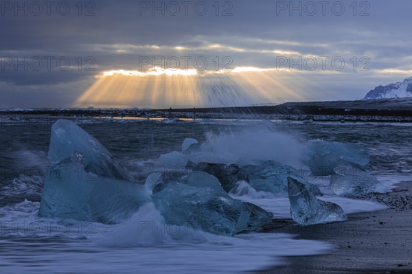 Waves breaking on icebergs on the black beach of Breidamerkursandur, sunset, near Jökullsarlon, Sudurland, Iceland, Europe