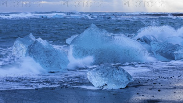 Waves breaking on icebergs on the black beach of Breidamerkursandur, near Jökullsarlon, Sudurland, Iceland, Europe