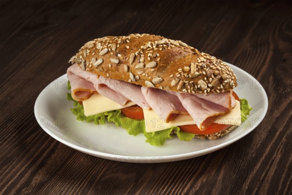 Ham sandwich with lettuce, cheese, tomato on plate on wooden table
