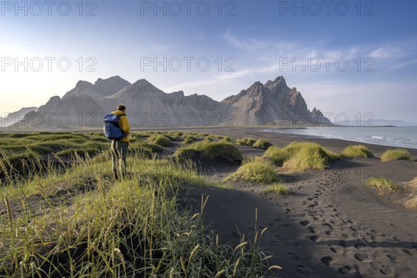 Tourist on a sand dune, Black beach with volcanic sand, Sand beach, Dunes with grass, Stokksnes headland, Klifatindur mountain range, Austurland, East Iceland, Iceland, Europe