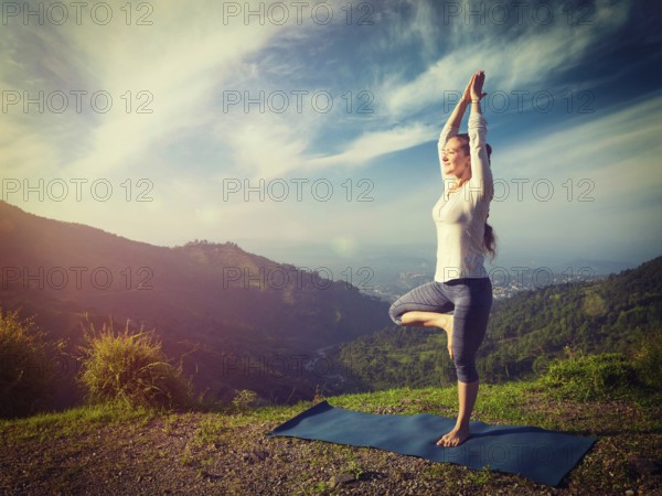Yoga practice outdoors, woman practices balance yoga asana Vrikshasana tree pose in Himalayas mountains outdoors in the morning. Himachal Pradesh, India. Panorama. Vintage retro effect filtered hipster style image