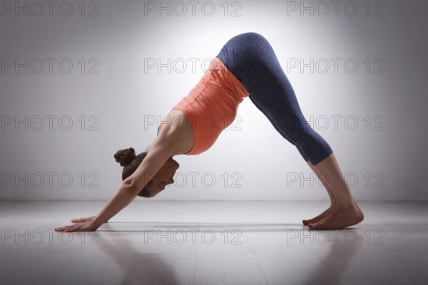 Beautiful sporty fit yogini woman practices yoga asana adhomukha svanasana, downward facing dog pose in studio