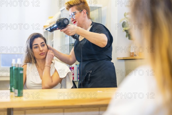Reflection on the mirror of hairdresser drying the hair of a client in the salon