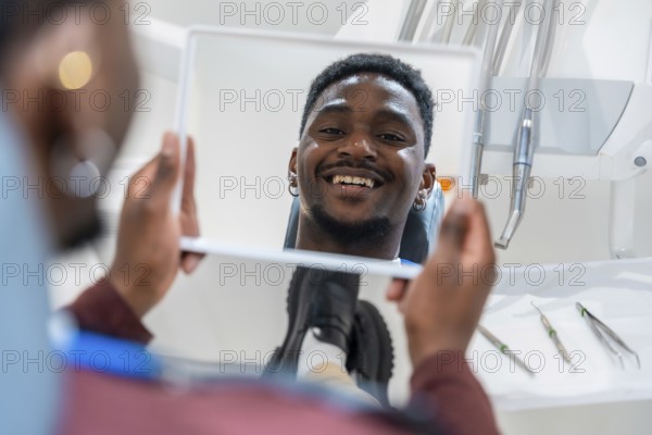 Happy patient looking at his whiter teeth in the mirror at the dental clinic after a whitening treatment