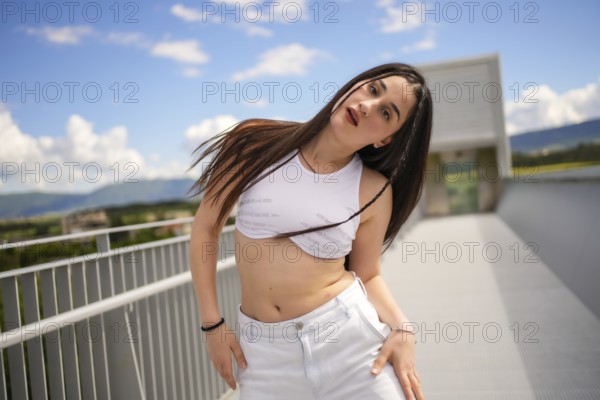 Caucasian young sportive woman moving sensually looking at camera while performing urban dance on an outdoor bridge