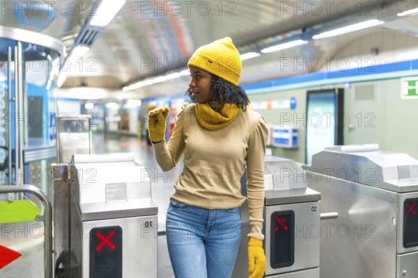 Young black woman wearing yellow winter clothes validating her ticket to enter subway station