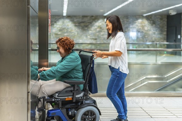Side view of a chinese female caregiver pushing wheelchair of a caucasiana adult disabled woman entering to metro elevator