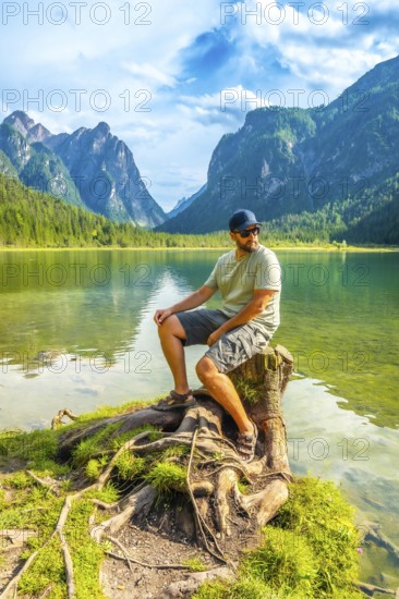Tourist enjoying the scenic view of lake dobbiaco and the dolomites mountains while sitting on a tree stump by the water