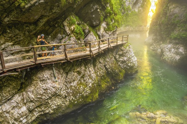 Tourists enjoying a scenic walk along the wooden pathway above the emerald radovna river, surrounded by the steep cliffs of vintgar gorge