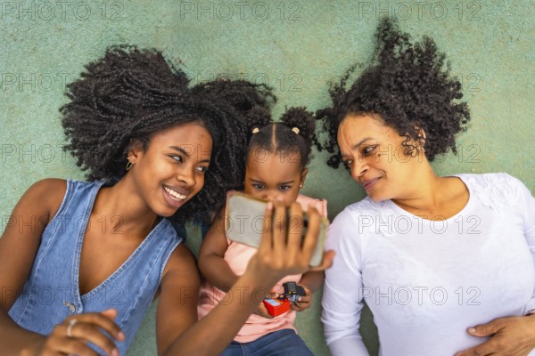 Top view of three african multi-generation woman watching the screen of the mobile lying down in a park