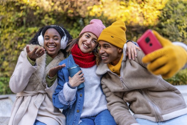 Three cheerful friends are taking a selfie in a city park, enjoying a winter day together