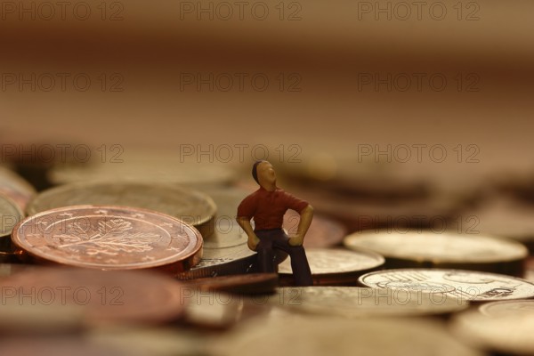 Miniature man sitting among euro coins, North Rhine-Westphalia, Germany, Europe