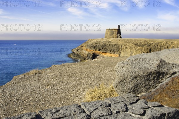 Coastal landscape with historic defence defence tower on a cliff and calm sea under a blue sky, Playa Blanca, Lanzarote, Canary Islands, Spain, Europe