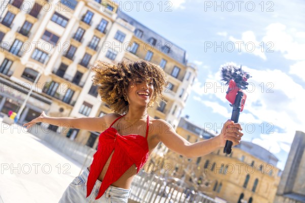 Dynamic photo of a happy latin young female vlogger streaming online using phone in the city