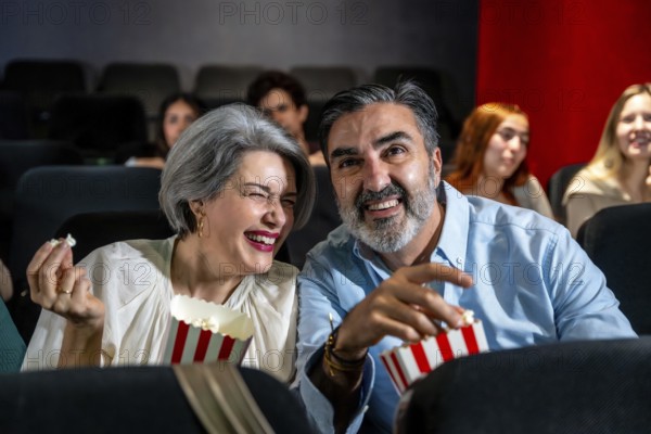 Mature couple having fun watching a comedy film at the movie theater, sharing popcorn and laughing together