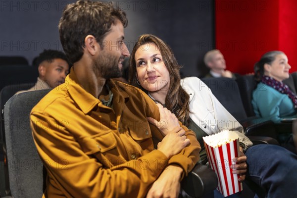 Couple enjoying a cozy movie night, sharing popcorn and affection while surrounded by a lively audience in a bustling cinema